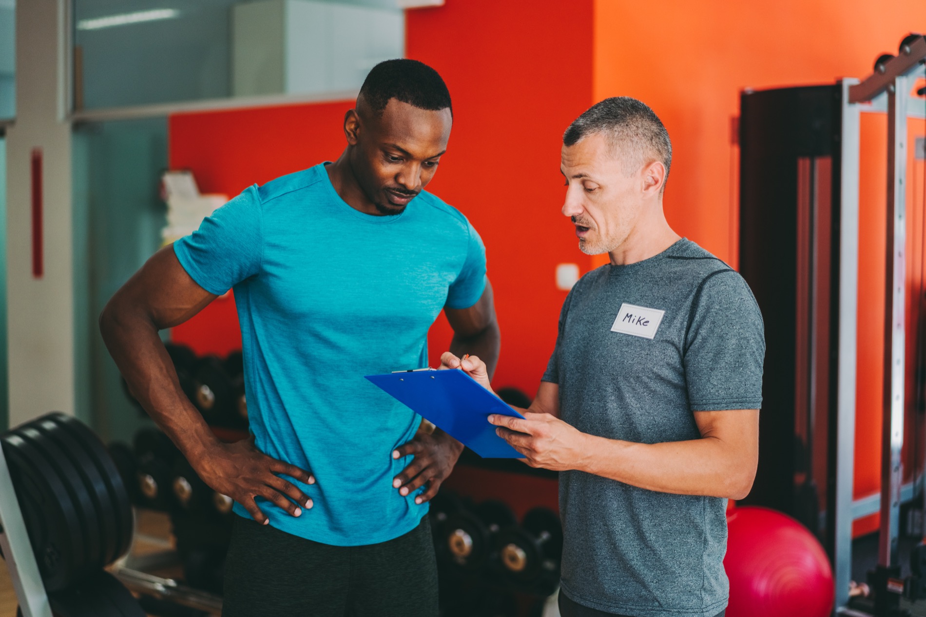 A personal trainer reviewing a program on a clipboard with his client
